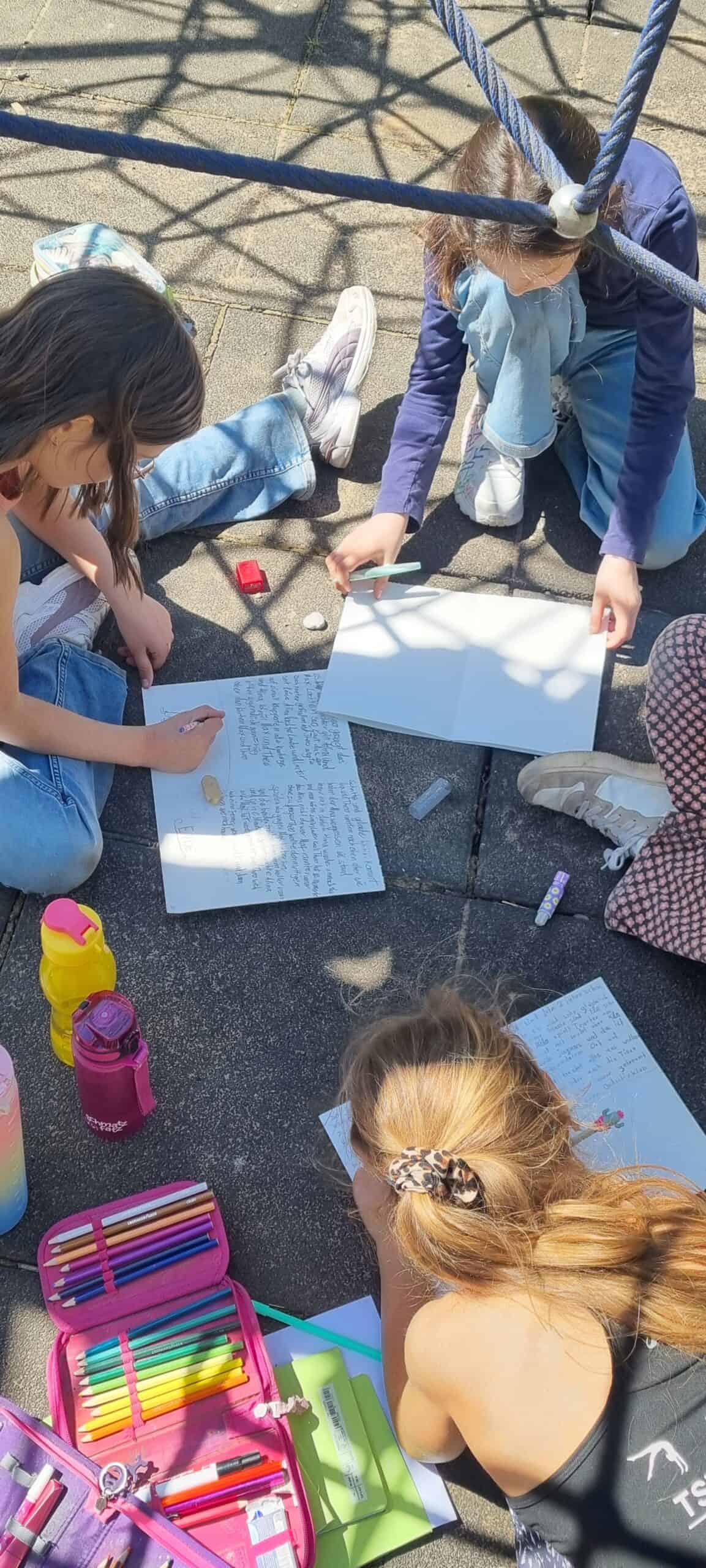 Kinder, die auf Betonboden sitzen und liegen und etwas auf Papier schreiben.