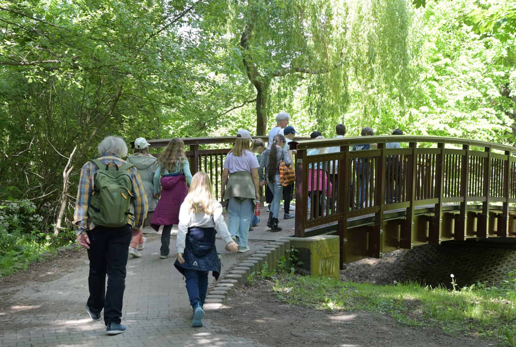 Eine Gruppe Kinder und ihre Begleitpersonen laufen über ein Brücke in einem Park.